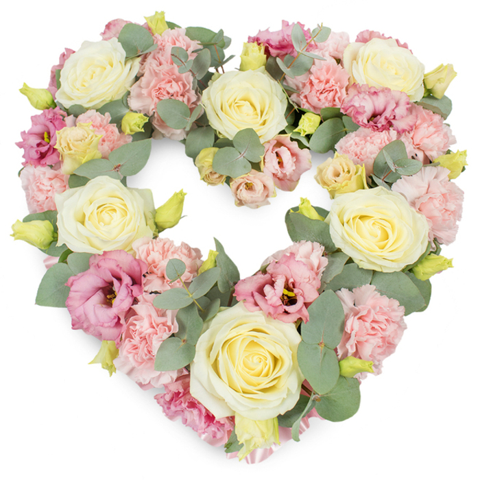 A beautifully composed heart-shaped floral tribute is shown against a bright white background, its dense, meticulously arranged blossoms creating a complete and symmetrical heart that reads instantly as a symbol of love and farewell, much like those seen at services around Blackheath and nearby Greenwich. The heart is fully covered with flowers, so that only petals and foliage are visible. Anchoring the design are large cream and soft buttery-yellow roses, each bloom formed from tightly layered petals that swirl from firm centres into open, velvety cups. These roses sit slightly above the rest of the design, lending the arrangement height and sculptural interest. Clustered between them are pastel pink carnations, their frilled, multi-layered petals overlapping to form soft, cloud-like patches of colour, adding a comforting, tactile quality. Richer tones appear in the magenta and mauve lisianthus that are woven throughout the heart; their trumpet-shaped blooms, some fully open and others gently unfurling, give the tribute depth and subtle shadows. Silvery-green eucalyptus leaves are threaded through the flowers, their smooth, rounded foliage outlining the heart's curves and creating a gentle contrast with the pastel petals. These leaves suggest a cool, crisp fragrance, reminiscent of a morning walk across Blackheath Common with the air fresh and still. Tiny yellowish-green buds peek between the larger blooms, offering hints of new life amid remembrance. The palette of cream, blush pink, soft yellow, and muted green produces a soothing, contemplative mood. Crafted with the attention to detail of an experienced local florist, this heart-shaped wreath is a fitting choice for funerals, chapel of rest visits, or memorial anniversaries, carrying a message of enduring affection and quiet, heartfelt condolence.