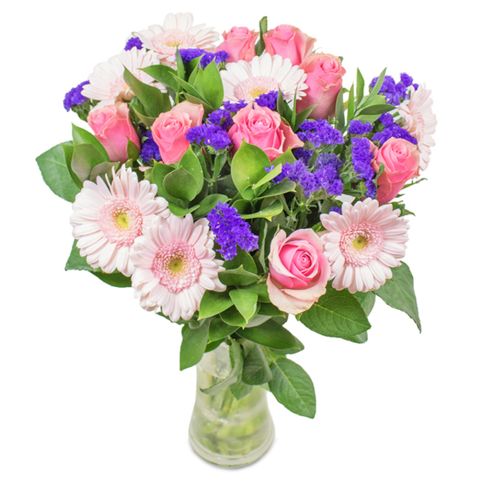 Set against a pristine white backdrop, this eye-catching bouquet from Blackheath Flowers captures the understated elegance and vibrant spirit of its neighbourhood. The centrepiece features around seven to nine pink roses, petals in various stages from tightly furled to just opening, each revealing its classic spiral and depth of colour. They're gracefully complemented by five to seven pale pink gerbera daisies, recognised by their captivatingly large, circular heads with almost white, luminous centres, adding a fresh, modern twist. Scattered among the primary blooms, clusters of deep purple statice provide a striking textural counterpoint and infuse the arrangement with dynamic energy, much like the summer wildflowers that line the walking paths near Blackheath Common. Lush deep green foliage completes the composition, delivering a sense of fullness and the lively freshness of a South London morning. With clean stems visible in a clear glass vase, the ensemble hints at the care and attention Blackheath Flowers brings to every bouquet. Whether for a birthday, an anniversary, Mother's Day, or as a stylish gift to lift the mood of a local office or home, this arrangement embodies joyful celebration, affection, and a deep connection to the Blackheath community.