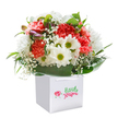 Joy radiates from this vibrant bouquet, gathered with a local Blackheath touch and presented in a crisp white carrier bag. The star here is a harmonious mingling of coral, pink, and ruby red carnations, their lavish, layered petals promising both exuberance and a whisper of sweet scent. Bright white daisies peer out from the folds, their cheerful golden-green hearts offering a smile as warm as a Saturday morning at the Blackheath Farmers' Market. Cloudlike sprigs of airy Gypsophila are scattered throughout, softening the bouquet and adding innocence-recalling the tranquil atmosphere found wandering through Greenwich Park nearby. Deep green, glossy foliage envelops the base, its wide leaves an anchor of elegance and vitality. Subtle hints of lavender-tinged buds nestle on one side, poised to blossom anew and lend a quiet intrigue to the rounded form. Everything is arranged with exceptional care in a sturdy white bag with simple ribbon handles, making it as suitable for easy delivery to Shooters Hill Road as it is for a heartfelt handoff at the door. The entire arrangement glows with morning light and freshness, the colours and textures captured with professional finesse. This bouquet is a celebration in itself-ideal for birthdays, moments of gratitude, or simply adding a spark of Blackheath's lively community spirit to any day.