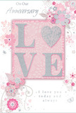 In this detailed view of an anniversary card, the design evokes the feeling of a hand-crafted bouquet from a trusted Blackheath florist. At the centre is the word LOVE, spelled out in tall, raised letters that stand above the surface of the card. Each letter is dusted with a soft, glittering finish, so they shimmer in pearly whites and silvery tones against a blush-pink panel, creating a focal point that catches both eye and touch. Flowing outward from the central word, illustrated flowers and curving vines sweep across the card in graceful arcs. The blossoms are stylized rather than literal, drawn in fine lines and shaded with gentle blush pink, pale grey, and tiny accents of silver, as if reflecting the muted, romantic hues of the heath at sunrise. Their arrangement feels instinctive and fluid, much like the way stems and foliage naturally fall into place in a carefully tied anniversary bouquet ready for delivery near the station or the village streets. The soft pink background provides a calm, even field of colour, allowing the glittered lettering and intricate floral pattern to stand out with a sense of depth. Elegant cursive script, placed thoughtfully on the card, conveys heartfelt anniversary sentiments about shared years and enduring love, written in a style that feels personal and sincere, almost like a message penned at a kitchen table overlooking Blackheath. Together, the pastel colours, tactile shimmer, and flowing floral lines create a card that radiates intimate celebration and quiet joy, perfectly suited for marking a treasured anniversary in this characterful London neighbourhood.